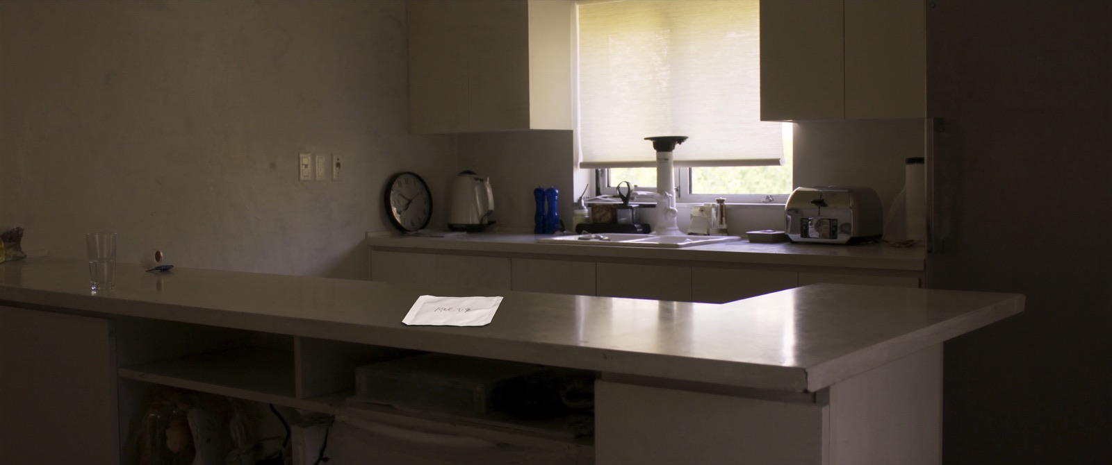 A single unmarked sachet and a glass of water on a kitchen counter in morning light.